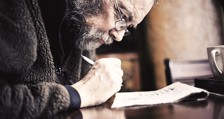 A bearded and bespectacled man peers closely at the crossword in the newspaper.