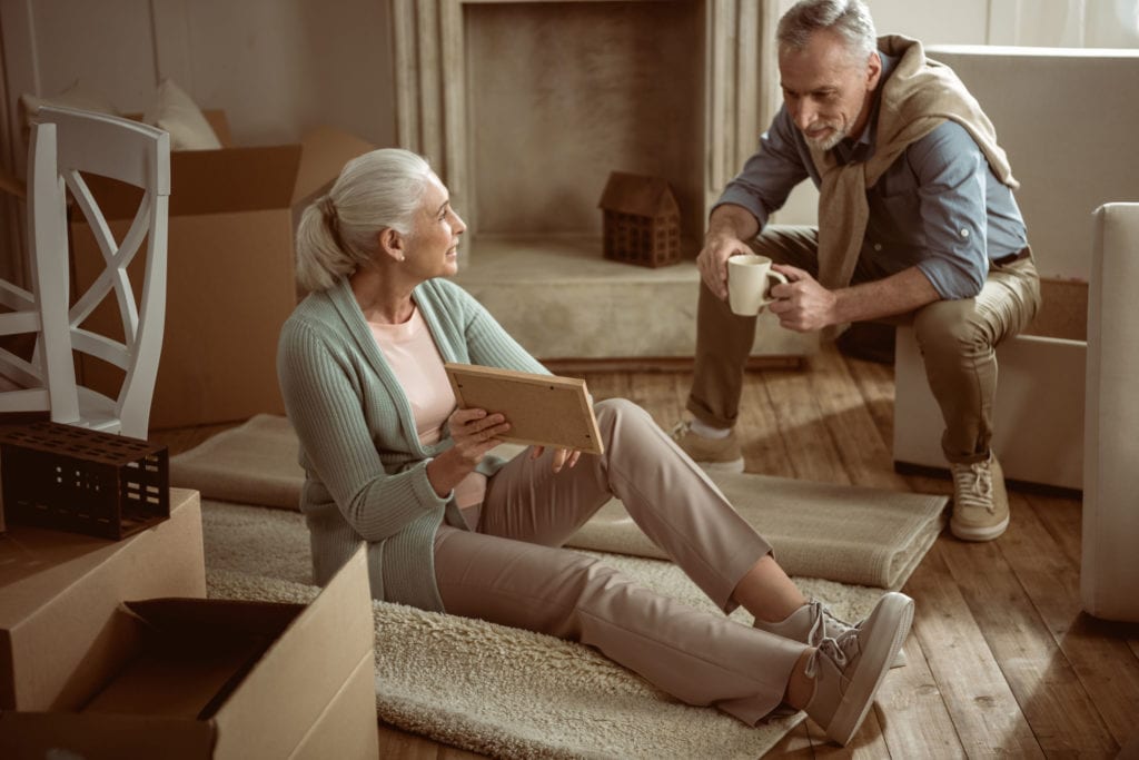 A woman sat on the floor, showing her husband a picture frame while packing to move houses