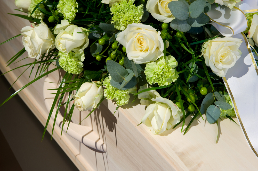White roses and green plants over part of a coffin
