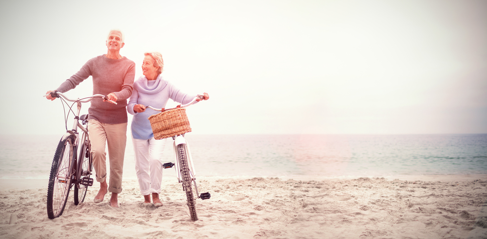 Elderly couple walking along the beach with bikes