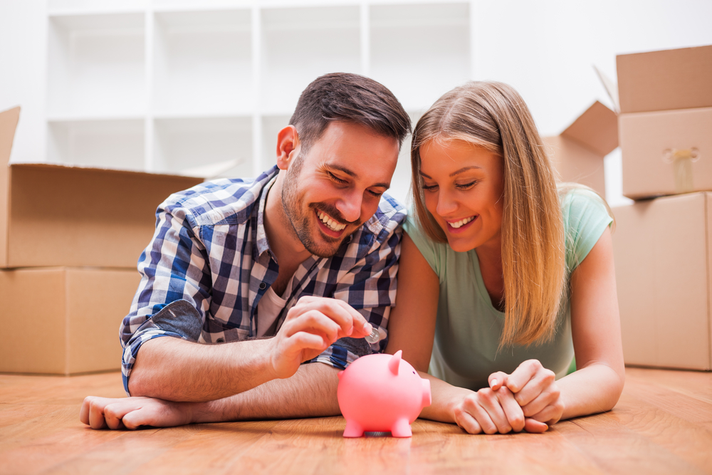 A man and women putting coins into a pig money box with boxes around them