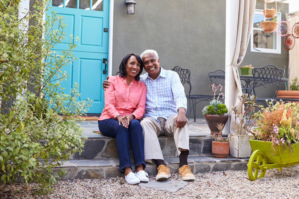 Elderly couple sat on the doorstep of their home, smiling