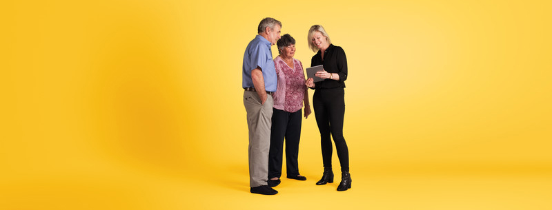 DevelopImages_OF_Brand2_-808_Yellow_BG (002) long landscape Woman showing mature couple something on a tablet