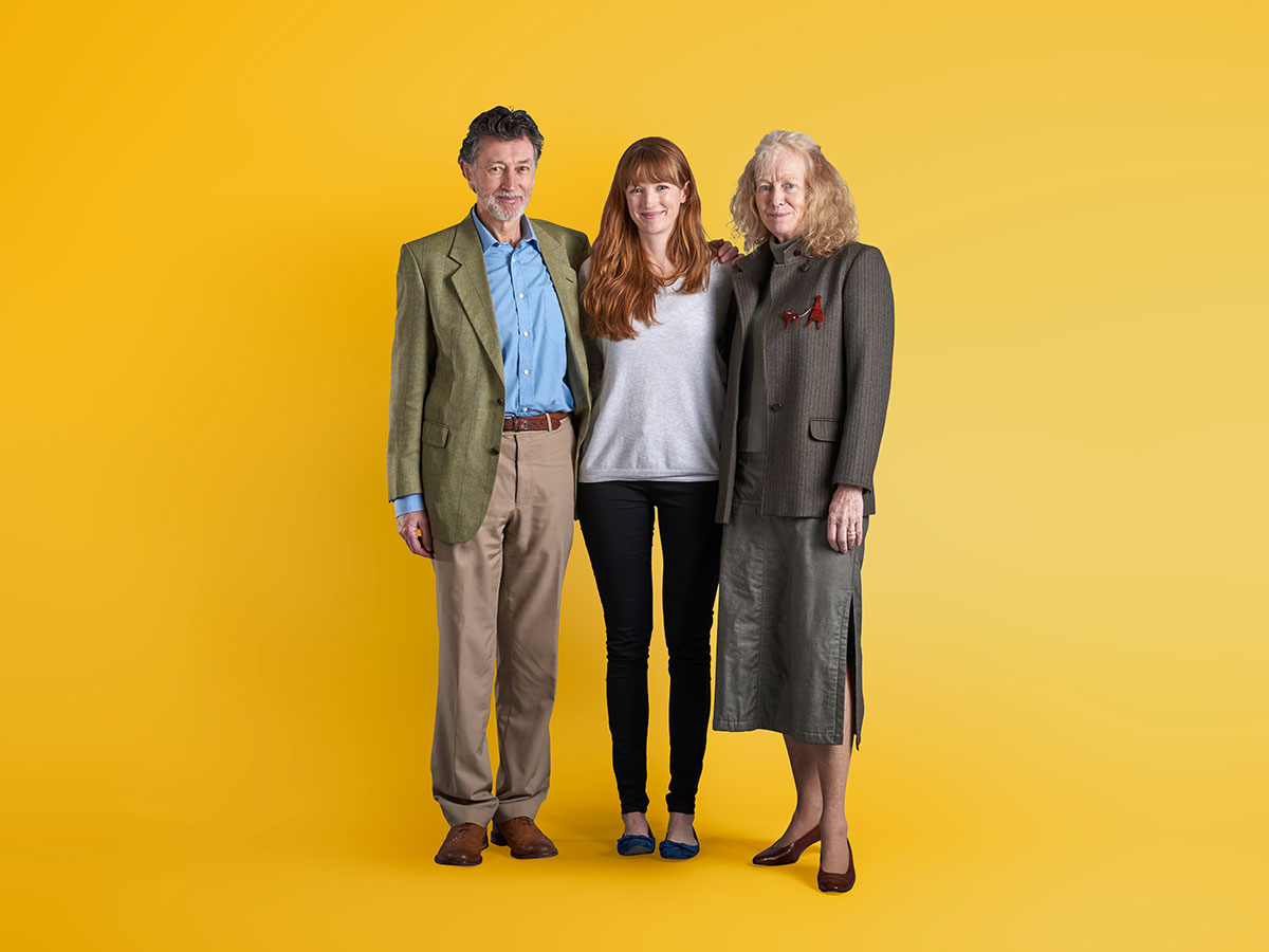 ofa-parents-daughter-yellow-1200x900 A fmother and father with their adult daughter against a yellow background