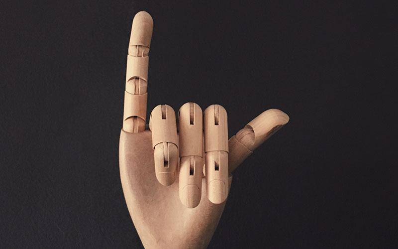 The wooden hand of a marionette, with it's pinky finger up and thumb pointing outwards.