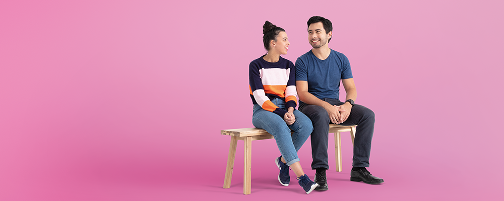 lisa-couple-bench-pink-1000x400 Two young adults sitting on a bench against a pink background