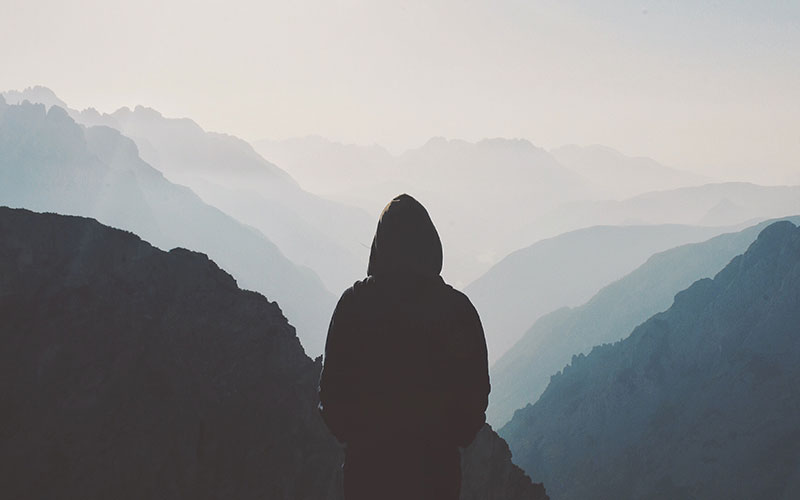 A hooded figure standing at the peak of a mountain valley.