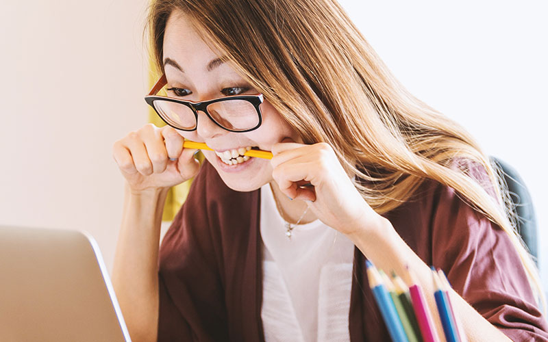 A woman using a laptop under stress, biting down on to a pencil.