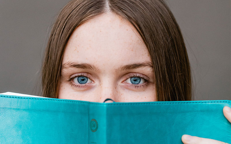 A young woman peering over the top of a book