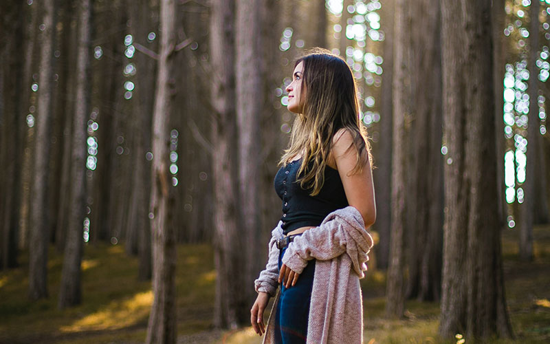 how-teens-are-becoming-greener-thinkers-800x500 A woman standing in a forest, with the sun shining over her.