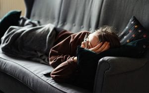 A child, wearing glasses, sleeping on a sofa, with a blanket.