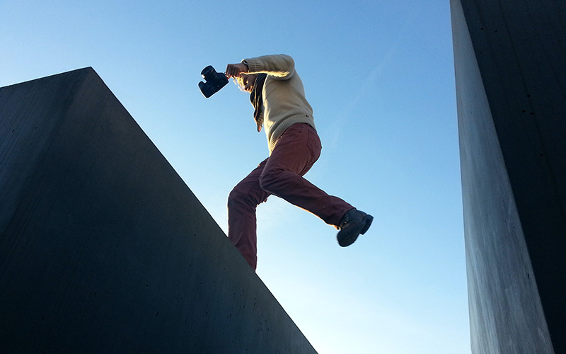 A man holding a camera, jumping over a small gap.