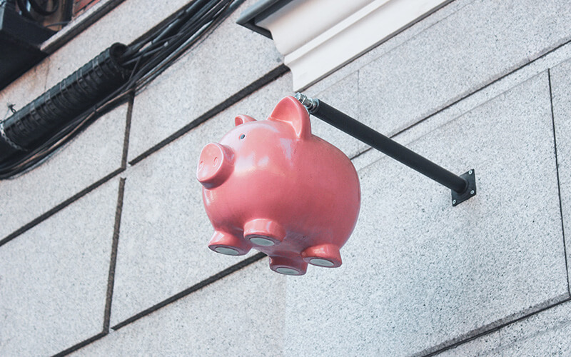 A piggybank suspended in the air, in front of a grey brick wall.