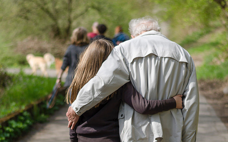 An elderly father walking down a path with his daughter