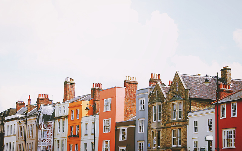 A row of houses, with a white cloudy sky behind them.