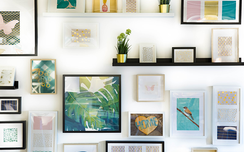 A neatly organised wall with many picture frames and a shelf with a plant pot.