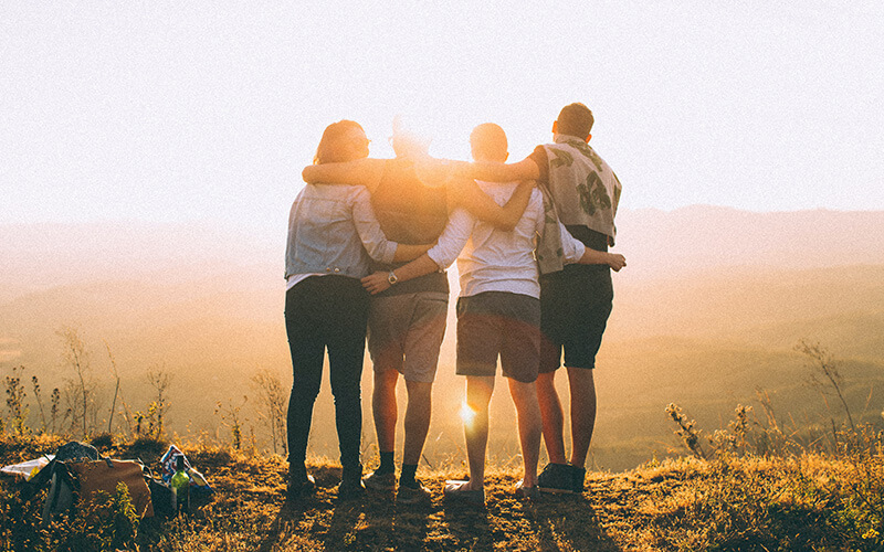 A group of four people huddled together looking at the sunset.
