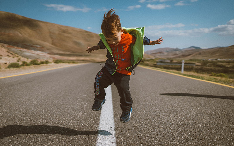 A child standing in the center of an empty road, jumping and smiling.