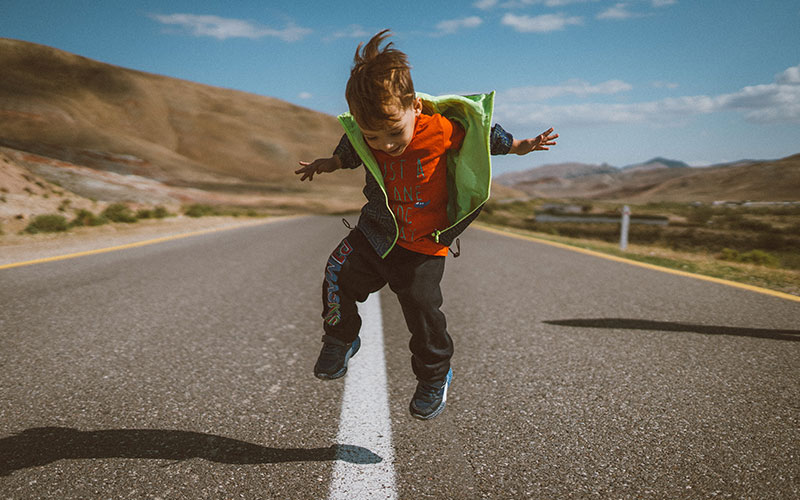 childrens-savings-guide-800x500 A child standing in the center of an empty road, jumping and smiling.