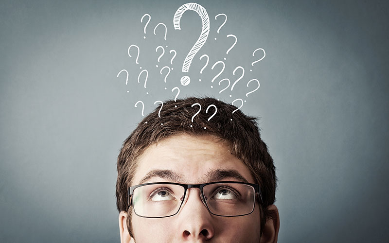 financial-jargon-buster-800x500 A man wearing glasses, thinking and looking upwards. Above him float question marks.