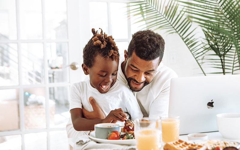 A father and son laugh together as they eat breakfast and make a financial plan for the family.
