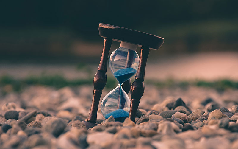 long-term-saving-800x500 An hourglass sitting on pebbles.