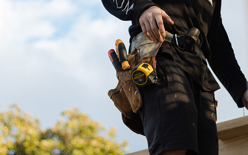 Tradesman standing outside, wearing a toolbelt.