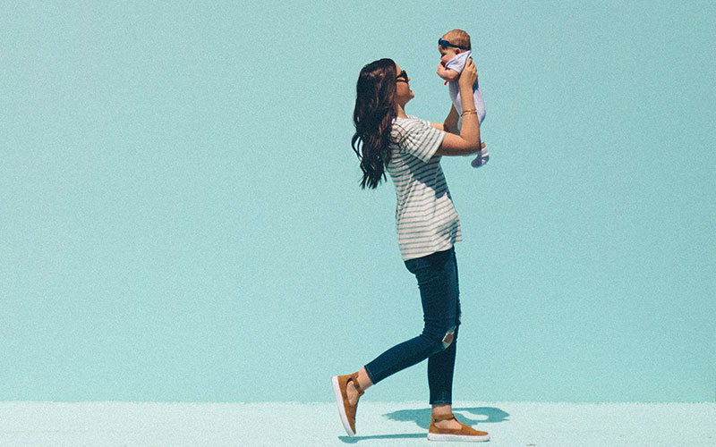 A woman holding her baby in the air, in front of a blue painted wall.