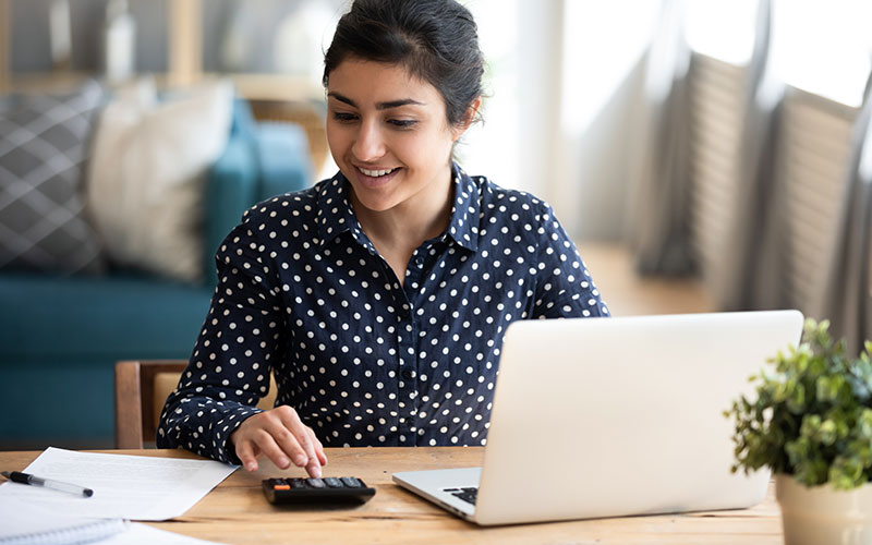 A woman sitting at a woman desk, using a calculator and a laptop.