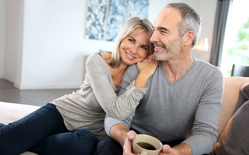 A middle-aged couple, laughing while sitting in their home.