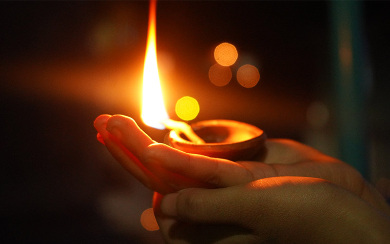 Two hands holding up a bright candle at night.