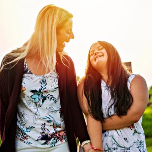 A mother and daughter standing side by side, laughing. A golden sky sets behind them.