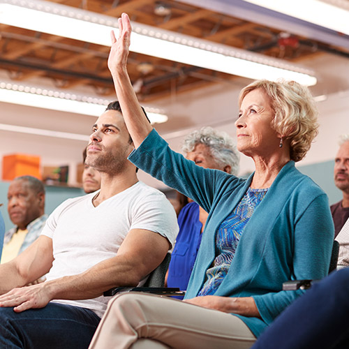 annual-general-meeting-500x500 A mature lady holding her hand up during a busy meeting