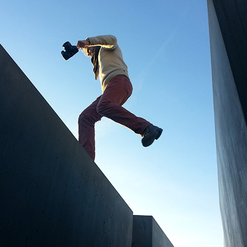 A man holding a camera, jumping over a small gap.