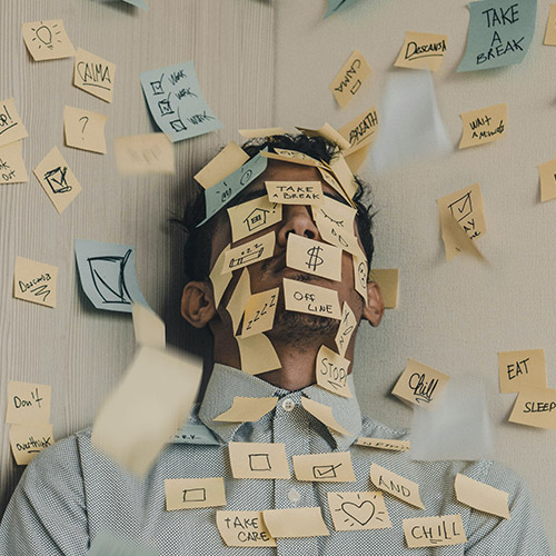 divorce-and-your-finances-500x500 A bearded man laying down, overwhelmed by dozens of sticky-notes stuck to his face, each containing a responsibility.