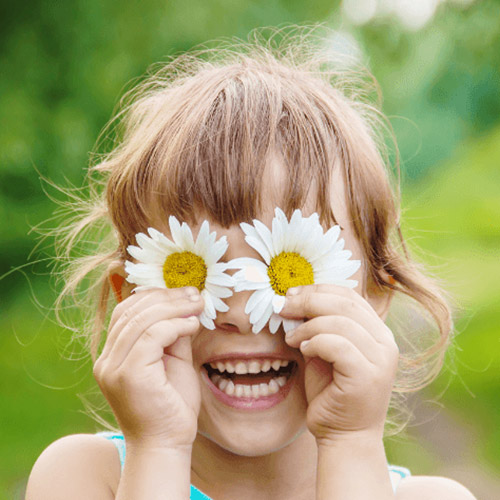 A little girl, with a big smile, covering her eys with flowers