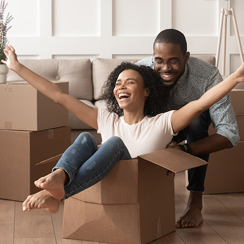 A man and woman having fun, pushing the woman along the floor in a cardboard box.