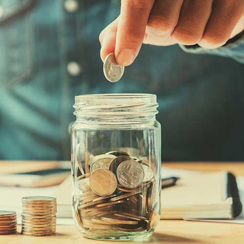 Top tips for long-term saving as a hand drops pennies in a glass jar