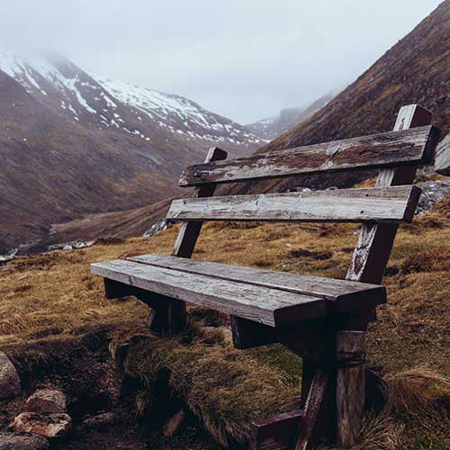 An old bench in the Highlands, surrounded by grass and snowy hills