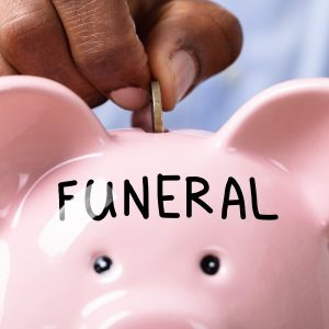 Money being put into a piggy bank with the word "funeral" written on it