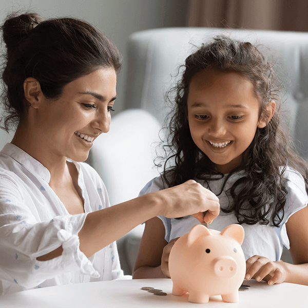 Smiling mother and young daughter putting coins in piggy bank