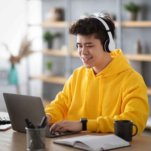 Teenager wearing headphones whilst smiling at laptop