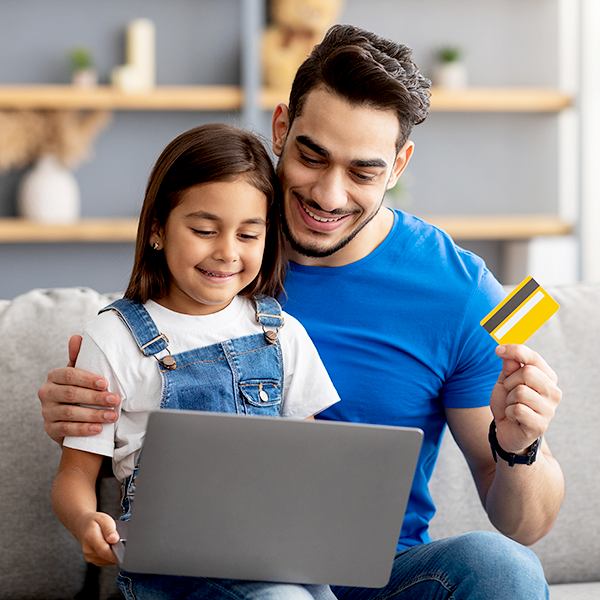Father and young daughter using laptop holding debit card