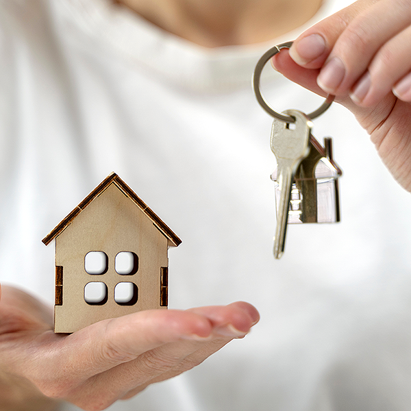 A person holding a wooden model house and a pair of keys.