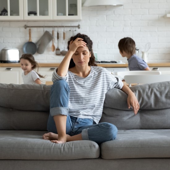 Woman sat on sofa looking upset while children play behind her