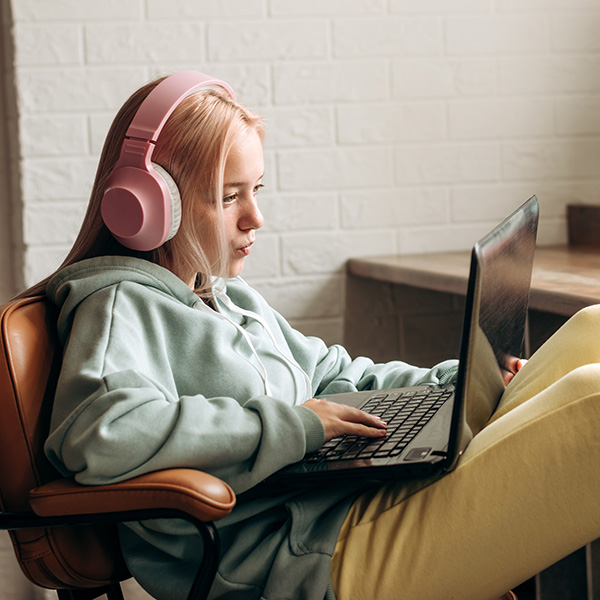 Pretty blonde teenage girl wearing headphones,using a laptop,doing homework at home.Back to school concept.School distance education at home during coronavirus pandemic,homeschooling,social media.