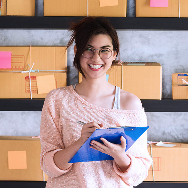 Young woman smiling and holding a clipboard in front of cardboard boxes