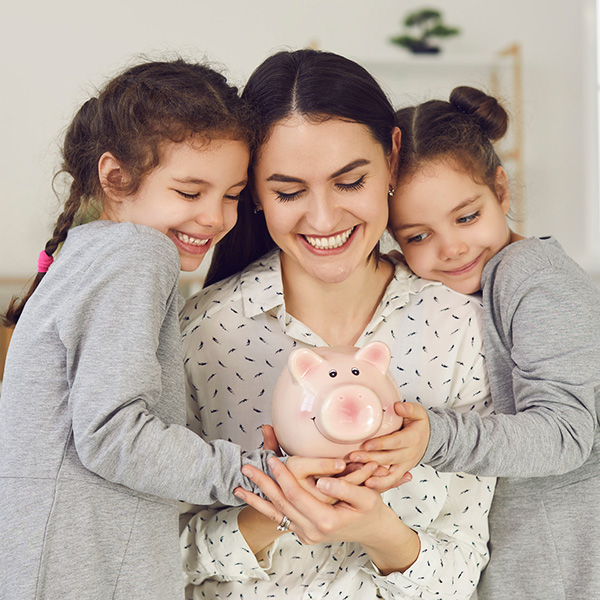 Smiling mother and young daughters holding a piggy bank