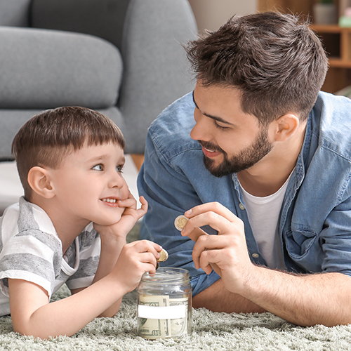 Little boy and father, smiling, putting money in a jar