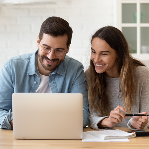 Happy couple sitting at a desk, looking at a laptop